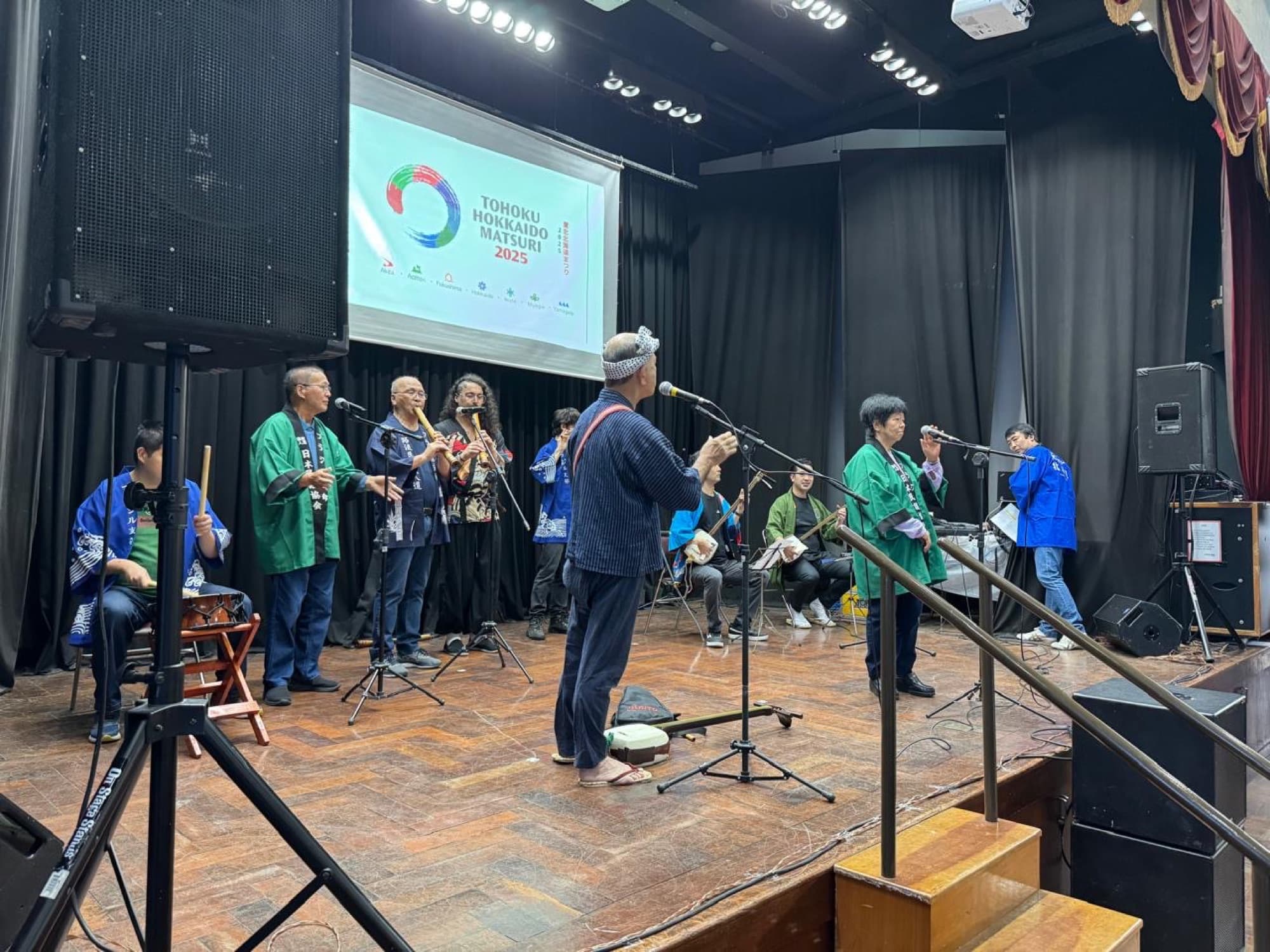 Apresentação musical no palco do Tohoku Hokkaido Matsuri 2025, com o logo do evento projetado ao fundo